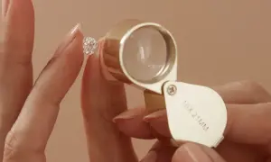 Eine Hand hält einen funkelnden Diamanten, während eine Lupe ihn vergrößert. Ein perfekter einschluss diamant wird genau geprüft.