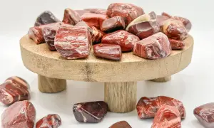 Rote und braune Jaspissteine, die die Bedeutung von Kraft und Vitalität symbolisieren, liegen auf einem Holzpodest und drumherum.