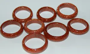 A collection of eight shimmering goldfluss stein rings, each a warm, coppery brown with flecks of gold.