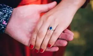 Ein Ring mit einem tiefblauen Saphir und kleinen Diamanten, gehalten von zwei Händen.
