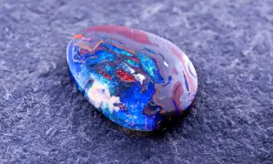 Ein faszinierender Edelstein aus Australien, ein Boulderopal, zeigt ein lebendiges Farbspiel aus Blau, Rot und Orange auf dunklem Grund.