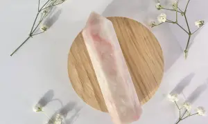 Ein polierter rosa Opal-Kristall liegt auf einem Holzsockel, umgeben von zarten weißen Blüten. Die rosa Opal Wirkung wird oft mit Liebe und Heilung assoziiert.