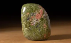 Ein glatt polierter Unakit-Stein mit grünen und rosa Flecken liegt auf einem Holztisch.