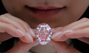 Hände halten einen rosafarbenen Diamanten. Welche Diamanten Farbe ist die teuerste? Rosa Diamanten sind extrem selten und wertvoll.