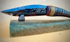 Ein Messer mit einer Klinge aus glänzendem, blau-braunem Obsidian, das an einem geschnitzten Holzgriff befestigt ist.