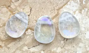 Drei tropfenförmige, klare Steine mit schillernden Regenbogenfarben, die an die angel aura wirkung erinnern, liegen auf einer marmorierten Oberfläche.