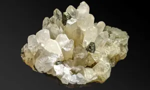 Ein Cluster aus klaren Quarzkristallen mit eingelagerten dunklen Mineralien. Die Quarz-Bedeutung liegt in seiner Klarheit und Reinheit, die oft mit Energie und Heilung assoziiert wird.