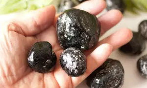 Eine Hand hält mehrere glänzende, schwarze Apachentränen-Steine. Sie sehen aus wie kleine, dunkle Tropfen.