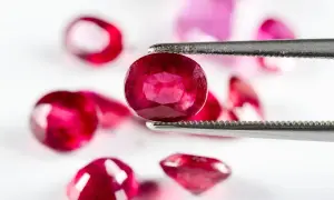 Ein Juwelier hält mit einer Pinzette einen tiefroten Edelstein, der wie der seltenste Diamant der Welt aussieht. Mehrere andere rote Steine liegen unscharf im Hintergrund.