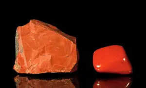 Zwei rote Jaspis-Arten: ein roher Stein und ein polierter Trommelstein, die auf schwarzem Hintergrund reflektieren.