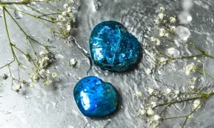 Zwei herzförmige Apatit Edelsteine glänzen unter Wassertropfen, umgeben von zarten weißen Blüten.