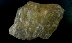 Ein gelblicher, schichtiger Stein, der an einen quarz katzenauge erinnert, liegt auf schwarzem Grund.
