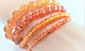 Armbänder aus leuchtenden, orange-roten Feuerachat-Kugeln in verschiedenen Größen, die wie ein warmer Sonnenuntergang auf der Haut liegen.