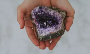 Hände halten einen tiefvioletten Amethyst. Seine Wirkung auf die Haut wird oft als beruhigend beschrieben.