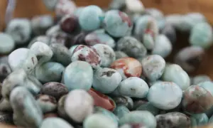 Haufen von glatten, polierten Larimar-Steinen in Blau- und Rottönen. Ihre beruhigende Larimar Wirkung soll Stress abbauen.