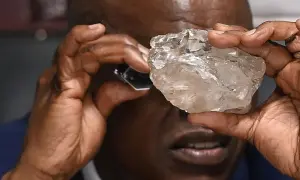 Mann betrachtet mit Lupe einen großen, rohen Diamanten. Die Frage, wie viele Diamanten es auf der Welt gibt, bleibt angesichts solcher Funde faszinierend.