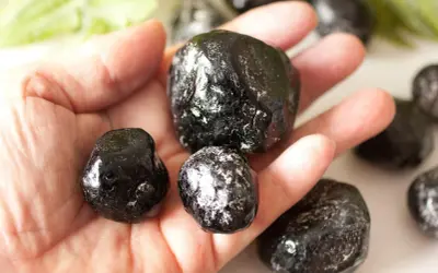 Eine Hand hält mehrere glänzende, schwarze Apachentränen-Steine. Sie sehen aus wie kleine, dunkle Tropfen.