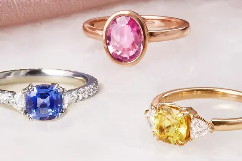 Drei Ringe mit Edelsteinen: ein blauer Saphir, ein gelber Saphir und ein rosa Saphir. Die Bedeutung von rosa Saphir steht für Liebe und Mitgefühl.