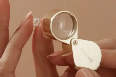 Eine Hand hält einen funkelnden Diamanten, während eine Lupe ihn vergrößert. Ein perfekter einschluss diamant wird genau geprüft.
