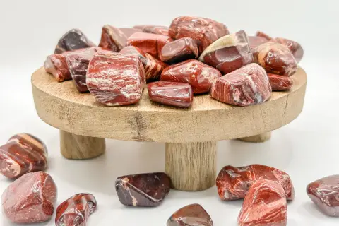 Rote und braune Jaspissteine, die die Bedeutung von Kraft und Vitalität symbolisieren, liegen auf einem Holzpodest und drumherum.
