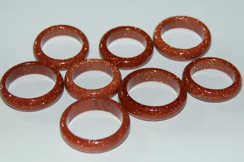 A collection of eight shimmering goldfluss stein rings, each a warm, coppery brown with flecks of gold.
