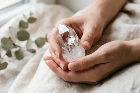 Hände halten einen facettierten Bergkristall, der Regenbogenfarben reflektiert. Die Bedeutung des Bergkristalls liegt in seiner Klarheit und Energie.