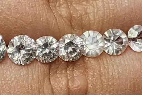 Reihe von geschliffenen Steinen, die auf einer Hautoberfläche liegen. Es ist schwierig, diamant oder zirkonia erkennen, da sie sehr ähnlich aussehen.