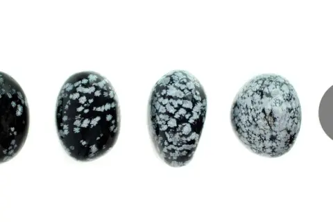 Vier polierte Steine aus schneeflockenobsidian, die wie kleine Eier geformt sind, liegen nebeneinander. Ein grauer Kreis rechts daneben.