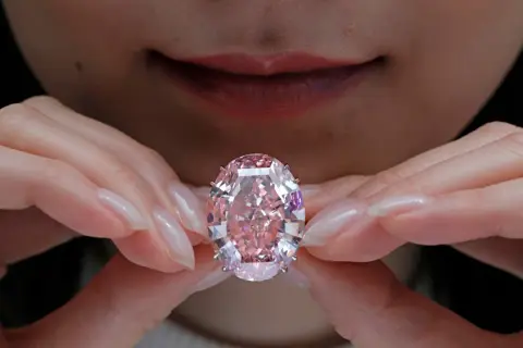 Hände halten einen rosafarbenen Diamanten. Welche Diamanten Farbe ist die teuerste? Rosa Diamanten sind extrem selten und wertvoll.