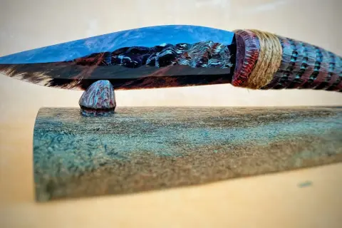 Ein Messer mit einer Klinge aus glänzendem, blau-braunem Obsidian, das an einem geschnitzten Holzgriff befestigt ist.