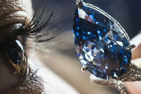 Ein Auge blickt auf einen funkelnden blauen Diamanten, dessen Wert unermesslich ist.