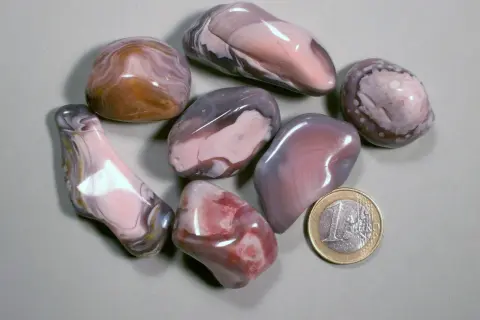 Glatt geschliffene Botswana Achat Steine in Rosa-, Grau- und Brauntönen, daneben eine 1-Euro-Münze.