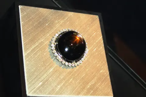 Ein glänzender schwarzer Saphir mit einem Stern-Effekt, umgeben von kleinen Diamanten. Seine geheimnisvolle schwarzer saphir bedeutung fasziniert.