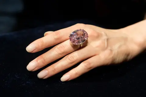 Ein großer, ovaler rosa Diamantring, der den teuersten Diamant der Welt Preis repräsentiert, wird an einer Hand getragen.