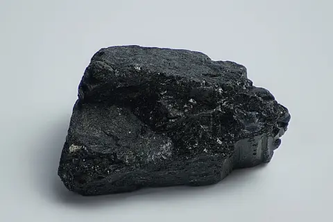 Ein glänzender, schwarzer Stein, der an einen Brocken Onyx erinnert, liegt auf weißem Grund.