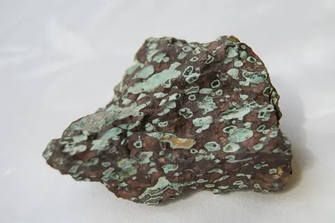 Ein roher, brauner Stein mit hellgrünen Einschlüssen, der an den Edelstein Türkis erinnert.