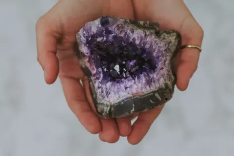 Hände halten einen tiefvioletten Amethyst. Seine Wirkung auf die Haut wird oft als beruhigend beschrieben.