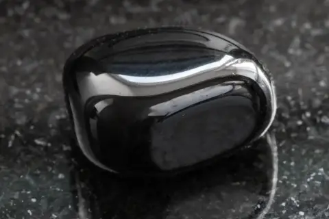 Glatter, glänzender onyx stein liegt auf einer dunklen, gesprenkelten Oberfläche.