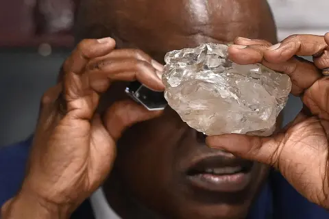 Mann betrachtet mit Lupe einen großen, rohen Diamanten. Die Frage, wie viele Diamanten es auf der Welt gibt, bleibt angesichts solcher Funde faszinierend.