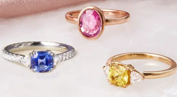 Drei Ringe mit Edelsteinen: ein blauer Saphir, ein gelber Saphir und ein rosa Saphir. Die Bedeutung von rosa Saphir steht für Liebe und Mitgefühl.