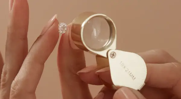Eine Hand hält einen funkelnden Diamanten, während eine Lupe ihn vergrößert. Ein perfekter einschluss diamant wird genau geprüft.