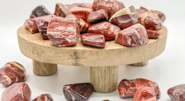 Rote und braune Jaspissteine, die die Bedeutung von Kraft und Vitalität symbolisieren, liegen auf einem Holzpodest und drumherum.