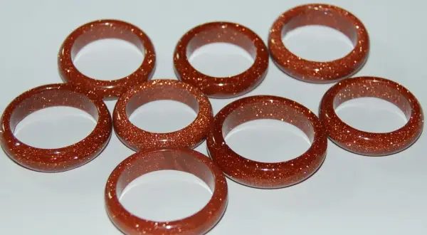A collection of eight shimmering goldfluss stein rings, each a warm, coppery brown with flecks of gold.