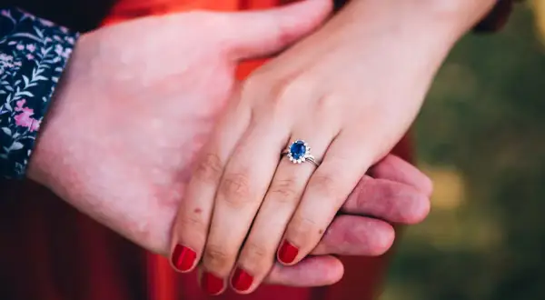 Ein Ring mit einem tiefblauen Saphir und kleinen Diamanten, gehalten von zwei Händen.