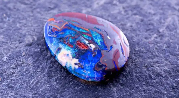Ein faszinierender Edelstein aus Australien, ein Boulderopal, zeigt ein lebendiges Farbspiel aus Blau, Rot und Orange auf dunklem Grund.