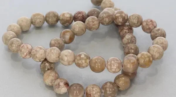 Zwei Stränge mit runden, beige-braunen Korallenperlen, die die Bedeutung von Schutz und Heilung symbolisieren.