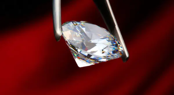 Ein funkelnder Diamant, gehalten von einer Pinzette, zeigt sein gesamtes Spektrum an Farben. Was ist ein brillant? Ein Stein, der Licht bricht und verzaubert.