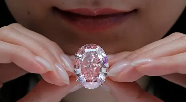 Hände halten einen rosafarbenen Diamanten. Welche Diamanten Farbe ist die teuerste? Rosa Diamanten sind extrem selten und wertvoll.