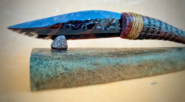 Ein Messer mit einer Klinge aus glänzendem, blau-braunem Obsidian, das an einem geschnitzten Holzgriff befestigt ist.