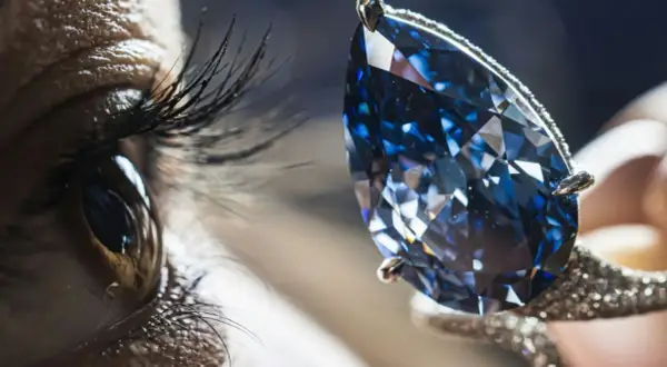 Ein Auge blickt auf einen funkelnden blauen Diamanten, dessen Wert unermesslich ist.